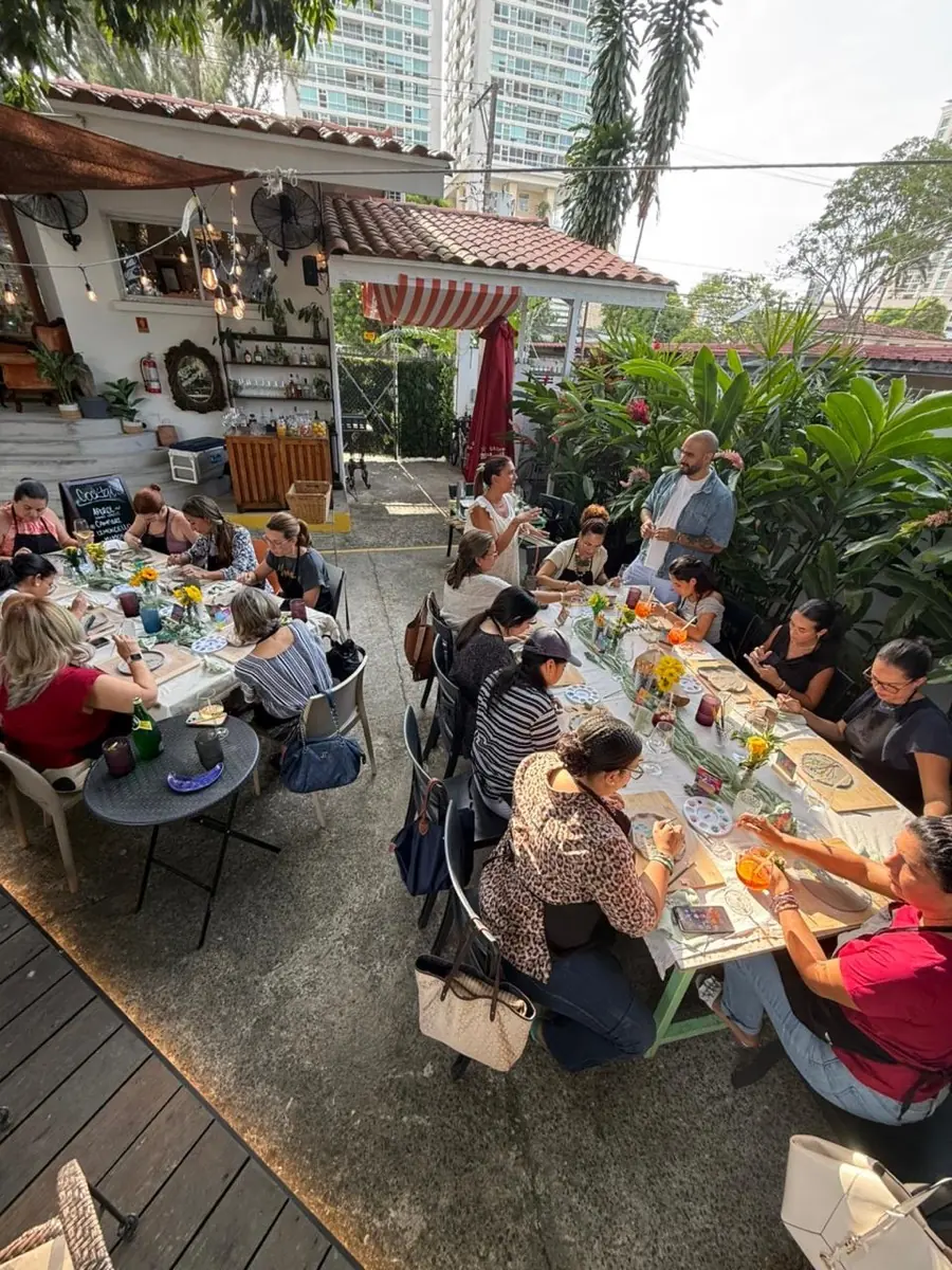 Evento privado de cerámica: invitados pintando piezas en una mesa larga bajo los árboles