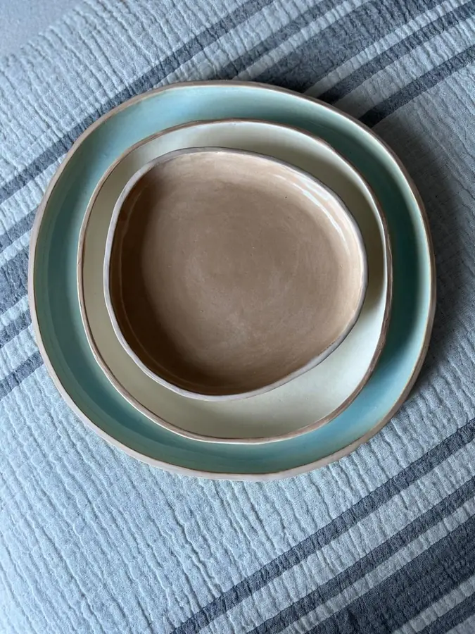 Plato y bowl de cerámica apilados en verde agua y arena sobre lino
